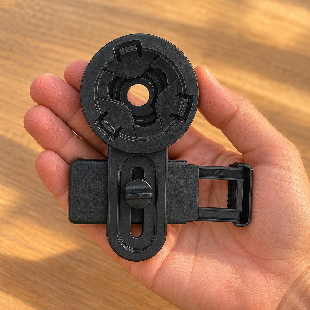Une main tient le support smartphone noir par son étrier, pince ouverte, au-dessus d'une table en bois